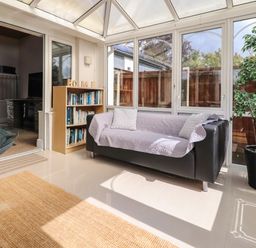 A sunroom with a black sofa covered with a light quilt next to a wooden bookshelf and a potted plant at Palm Court in Burton-in-Kendal