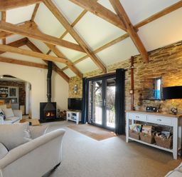 A living room with exposed wooden beams a wood burning stove sofas a wooden cabinet with baskets and a lamp at Lily Cottage in Looe