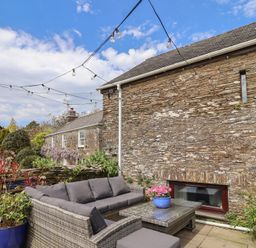 An outdoor seating area with a couch and flower pots at Lily Cottage in Looe