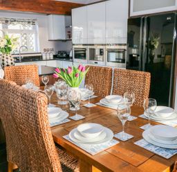 A kitchen with a wooden dining table set for six with woven chairs and a vase of tulips at Swn y mor in Amroth