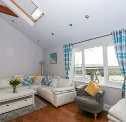 A living room with white leather sofas a grey armchair a white coffee table with flowers and blue check curtains at Swn y mor in Amroth