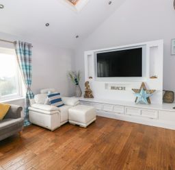 A living room with a gray armchair and a white leather chair next to a wall-mounted television and decorative items at Swn y mor in Amroth
