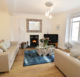A living room with beige sofas a glass coffee table a blue rug a fireplace and a large window at Waverley House in Beaumaris