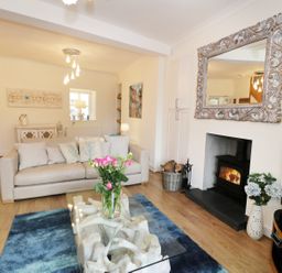 A living room with a beige sofa cushions a glass coffee table with flowers a fireplace and a large mirror at Waverley House in Beaumaris