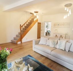A living room with a beige sofa and cushions near a wooden staircase and a glass coffee table with flowers at Waverley House in Beaumaris