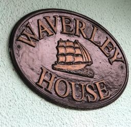 A metal sign with a ship and the words Waverley House mounted on a textured wall at Waverley House in Beaumaris