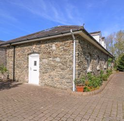 A stone building with a white door and windows surrounded by a paved driveway and plants at Fisher Granary in Lampeter
