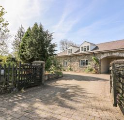 The exterior of a stone house with a paved driveway and a black wooden gate at Fisher Granary in Lampeter