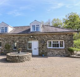 The exterior of a stone house with white windows and a white door next to a circular stone structure at Fisher Granary in Lampeter