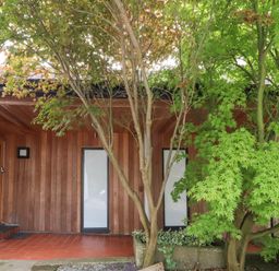 An exterior entrance area with wooden walls two tall windows and green trees at Underfell in Burton-In-Kendal