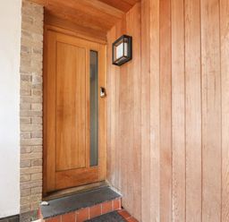 A wooden front door with a vertical glass panel and a keypad lock next to a brick wall and wooden panelled wall at Underfell in Burton-In-Kendal