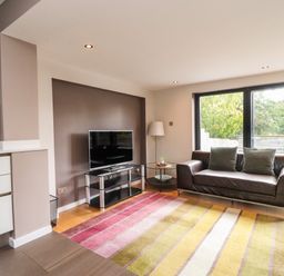 A living room with a brown leather sofa two cushions a TV on a stand a round side table and large sliding glass doors at Underfell in Burton-In-Kendal