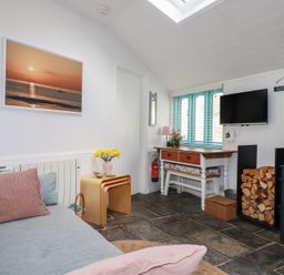 A living room with a sofa, television, and fireplace at Smugglers Cottage in Trebarwith Strand near Tintagel