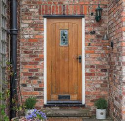 A wooden front door with a small window set in a brick wall with potted plants on either side at Manor Cottage in Northallerton