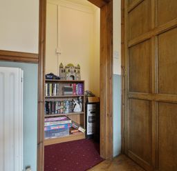 A small room with a wooden door a white radiator and a bookshelf filled with books board games and decorative items at Manor Cottage in Northallerton