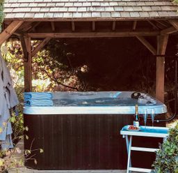 An outdoor hot tub under a wooden gazebo with robes hanging and a small table with champagne and glasses at Penlaurel in Launceston