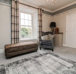 A sitting room with an armchair and ottoman near a window with checked curtains at Penlaurel in Launceston