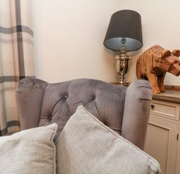 A gray upholstered armchair with beige cushions next to a cabinet with a lamp and wooden bear sculpture at Penlaurel in Launceston