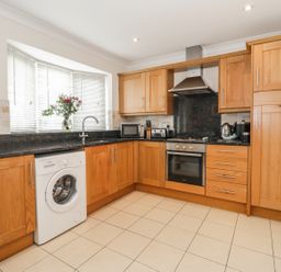A kitchen with wooden cabinets a washing machine an oven and a vase with flowers on the windowsill at Ladybird in Bridgwater