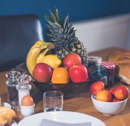 A dining table with a fruit bowl containing pineapple bananas lemon apples and an orange bread eggs salt and pepper at Ladybird in Bridgwater