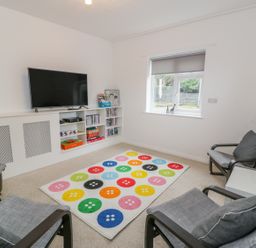 A sitting room with a wall mounted television four chairs a colourful button patterned rug and a window at Hendre Wylan in Llanaber