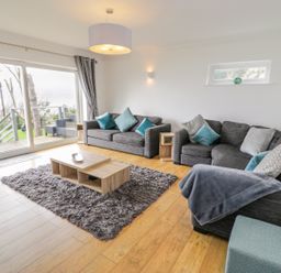 A living room with gray sofas and blue cushions beside a large glass door at Hendre Wylan in Llanaber