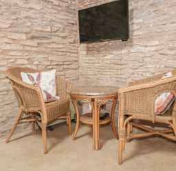 A corner seating area with two wicker chairs with cushions and a small round table under a wall-mounted TV at The Cow Cott in Hereford