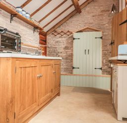 A kitchen with wooden cabinets a toaster oven a blue kettle and toaster and stone walls at The Cow Cott in Hereford