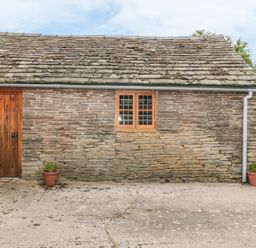 A stone building with a wooden door and window and two potted plants at The Cow Cott in Hereford
