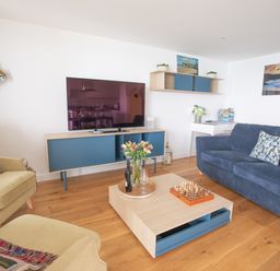 A living room with blue and beige furniture a tv on a blue and wooden stand and a coffee table with flowers and chess at Onshore 6 - Newquay Towan Beach View in Newquay