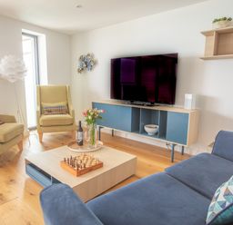 A living room with armchairs a sofa a coffee table with a chessboard flowers and wine a television on a cabinet and a floor lamp at Onshore 6 - Newquay Towan Beach View in Newquay