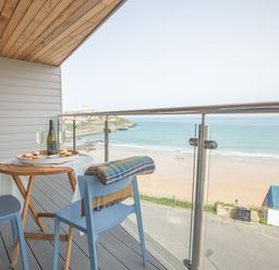 A balcony with a wooden table set with food and drinks and blue chairs overlooking a beach at Onshore 6 - Newquay Towan Beach View in Newquay