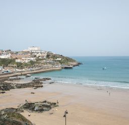 A beach with sand and rocks next to a coastal town and a small boat in the water at Onshore 6 - Newquay Towan Beach View in Newquay