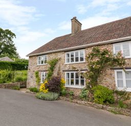 A stone cottage with white framed windows and climbing plants outside at Whitehall Farm Cottage in Honiton