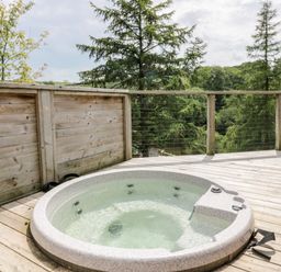 A wooden deck with a round hot tub overlooking trees at 6 Lake View in Lanreath