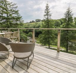 An outdoor wooden deck with wicker chairs and a table surrounded by trees at 6 Lake View in Lanreath