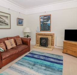 A living room with a brown leather sofa a blue striped rug a small fireplace a wooden TV stand with a television and framed pictures on walls at 11 Marine Terrace in Criccieth