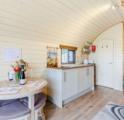A kitchen area with a small dining table and chairs inside a wooden pod at Corndon Pod White Grit near Chirbury