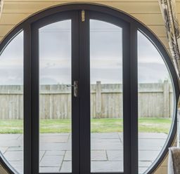 A circular black-framed glass door with patterned curtains and a view of a fenced yard at Stiperstones Pod in White Grit near Chirbury