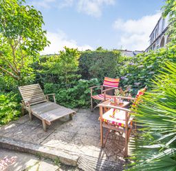 A garden patio with wooden chairs and a table surrounded by green plants at Downlea in Looe