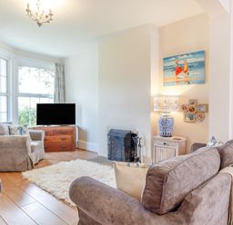 A living room with sofas a TV on a wooden chest a lamp and a painting at Downlea in Looe