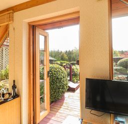 A room with a wooden door open to a garden patio and a television mounted on the wall at Swallow Lodge in Amble