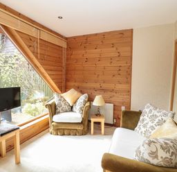 A living room with green armchairs and a sofa near a large window and a small wooden table with a lamp at Swallow Lodge in Amble