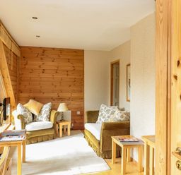 A sitting area with two armchairs a lamp and wooden side tables in a room with wooden paneling at Swallow Lodge in Amble