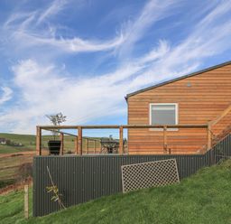 An outdoor deck with table and chairs attached to a wooden building with railing on a grassy hillside at Haka Lodge in Devil's Bridge