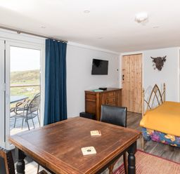 A room with wooden table and chairs a bed with floral bedding and a yellow blanket a wooden cabinet and sliding glass doors leading to an outdoor patio at Haka Lodge in Devil's Bridge