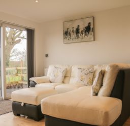 A living room with a beige and black sectional sofa and horse painting on the wall at Upham View in Woodbury