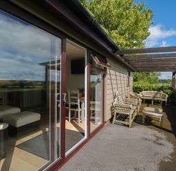 A patio with wooden chairs and a table outside a building with glass sliding doors at Upham View in Woodbury