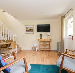 A living room with two armchairs a wooden table under a wall-mounted TV and a dining table near a staircase at Pugwash Cottage in Falmouth
