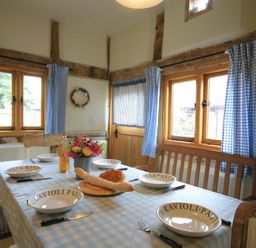 A dining area with a table set with bowls bread and flowers and blue checkered curtains at Whites Farm Barn in Ledbury